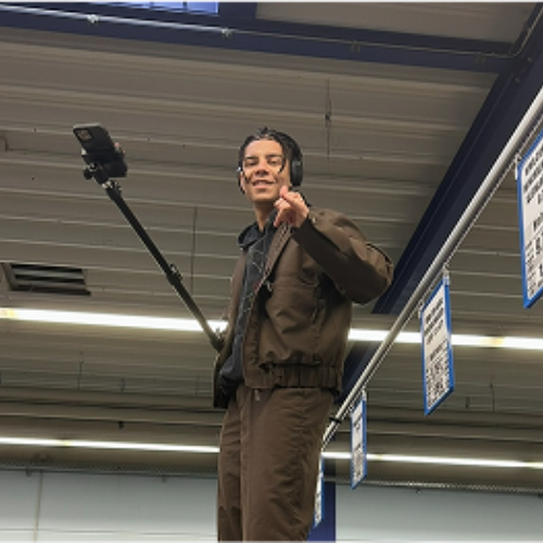 Benjamin steht auf einer Getr&auml;nkepalette mit einer Kamera in der Hand und winkt in die Kamera